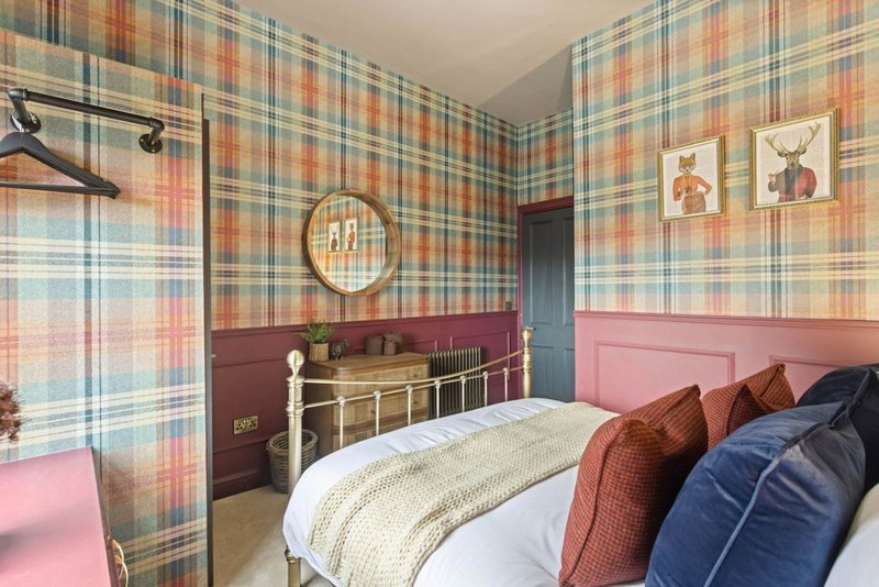 Bedroom with plaid wallpaper, metal bed frame, pink headboard and patterned cushions