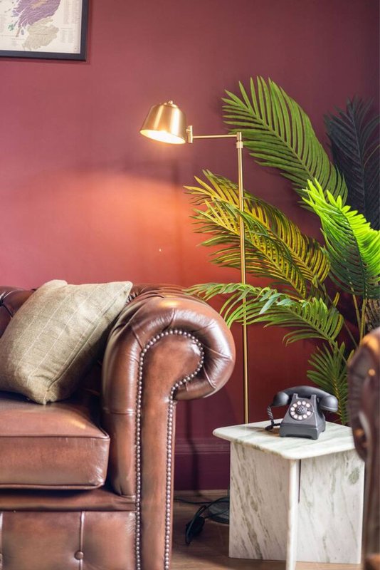 Living room with burgundy walls, leather Chesterfield sofa, brass floor lamp, potted plant and side table