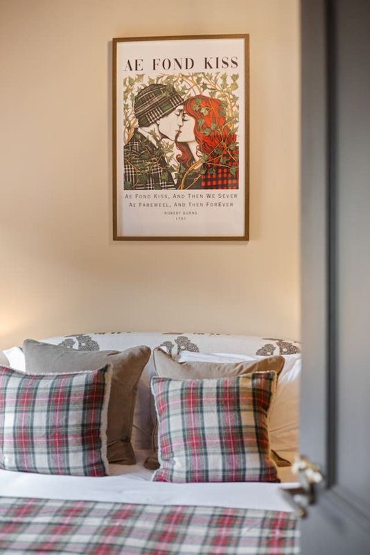 Bedroom with double bed, plaid pillows and bedding, framed vintage art poster above