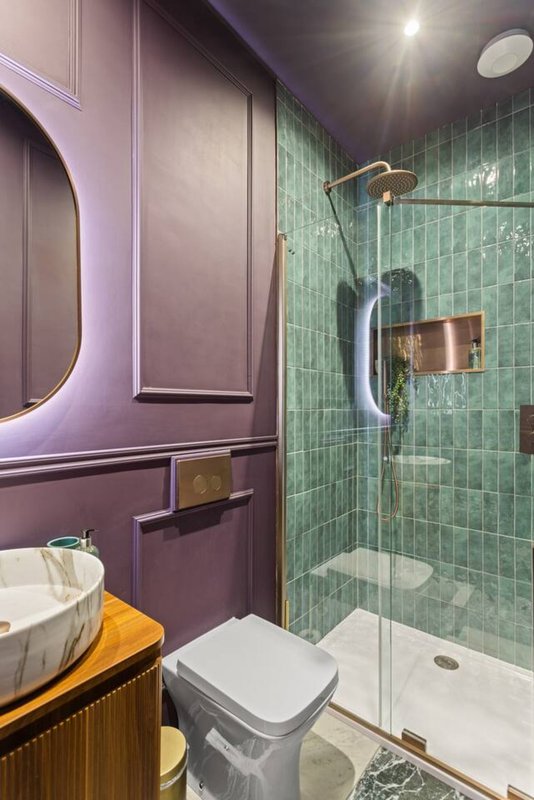Modern bathroom with purple cabinetry, green tile shower, round mirror and wooden vanity