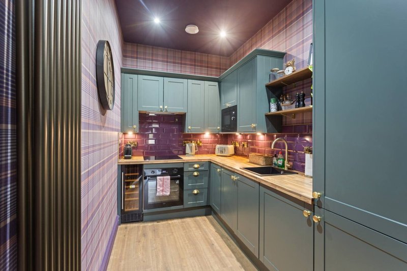 Modern kitchen with sage green cabinetry, purple tile backsplash, wooden countertops and integrated appliances