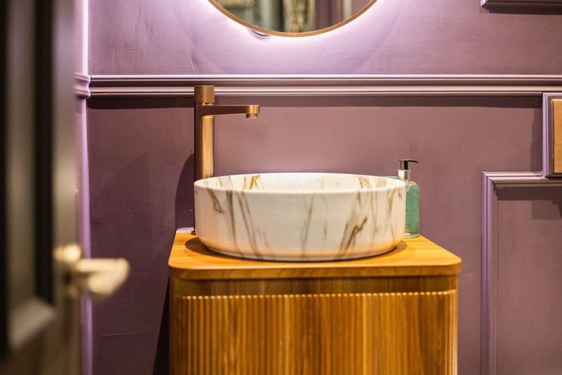 Modern bathroom with marble bowl sink on golden vanity unit and pink walls