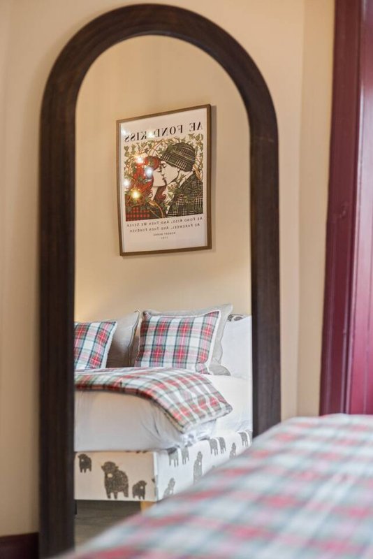 Bedroom mirror reflection showing bed with checkered bedding and framed poster on wall