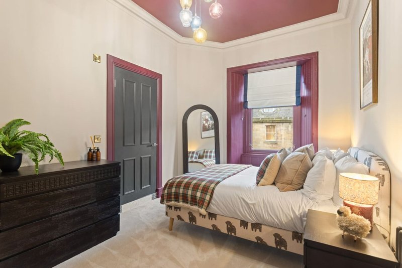 Bedroom with double bed, dark wood dresser, mirror, purple-framed doors and burgundy ceiling