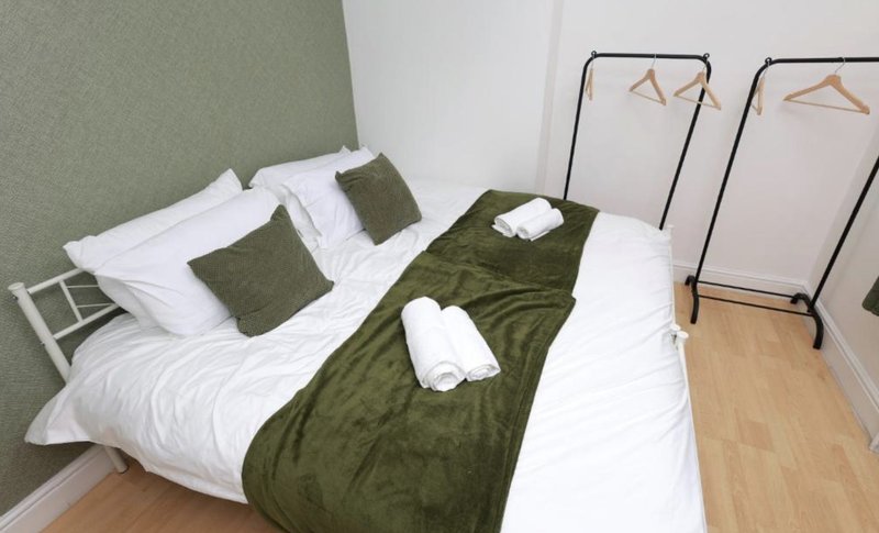 Alternative bedroom with double bed, olive green bedding, white pillows and wooden floor