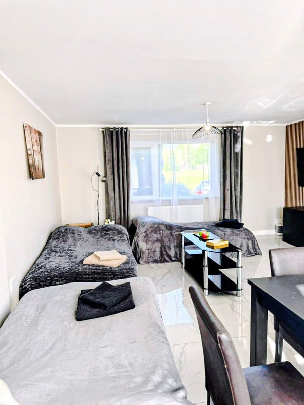 Modern bedroom with two single beds, black furnishings, large window with curtains and bright natural light