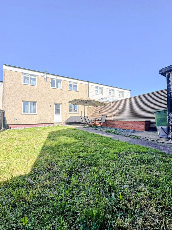 Rear garden view of two-storey brick house with patio, lawn and fence