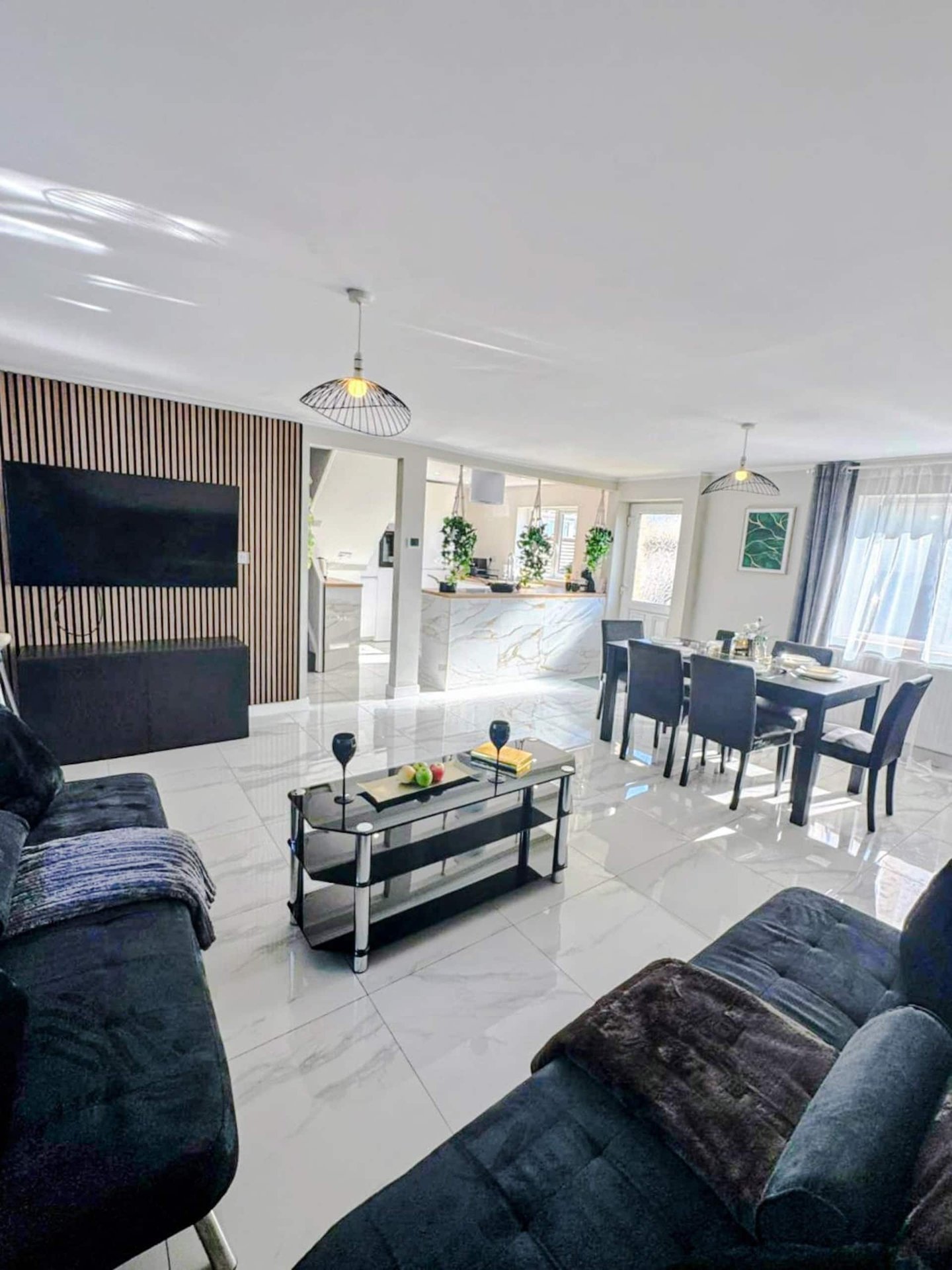 Modern open-plan living room with sofas, dining table, kitchen, and bedroom visible through archway