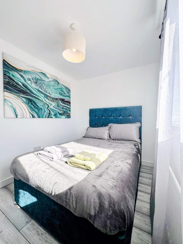 Bedroom with double bed, teal headboard, grey bedding, wall art and pendant light