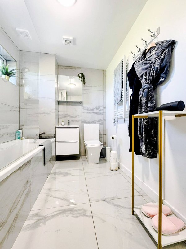 Modern bathroom with marble tiles, vanity sink, toilet, shower enclosure and towel rack