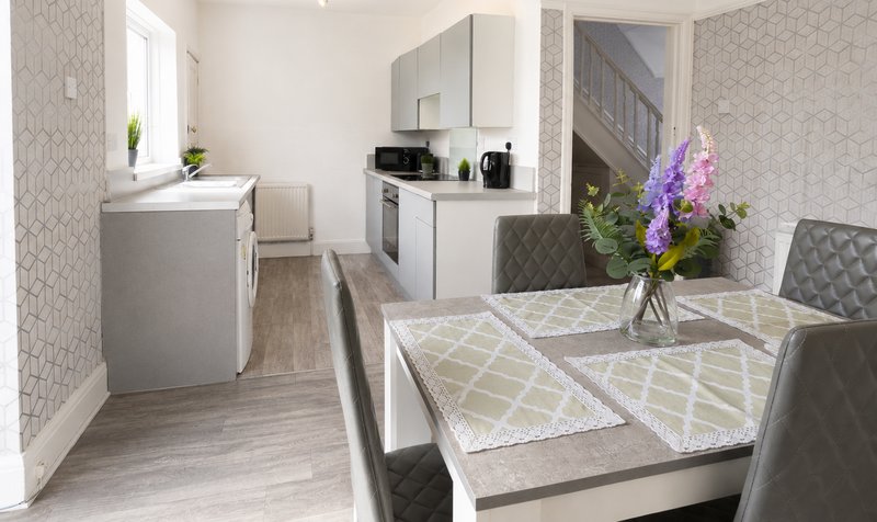 Modern kitchen-diner with white cabinetry, dining table, fresh flowers, and light wood flooring