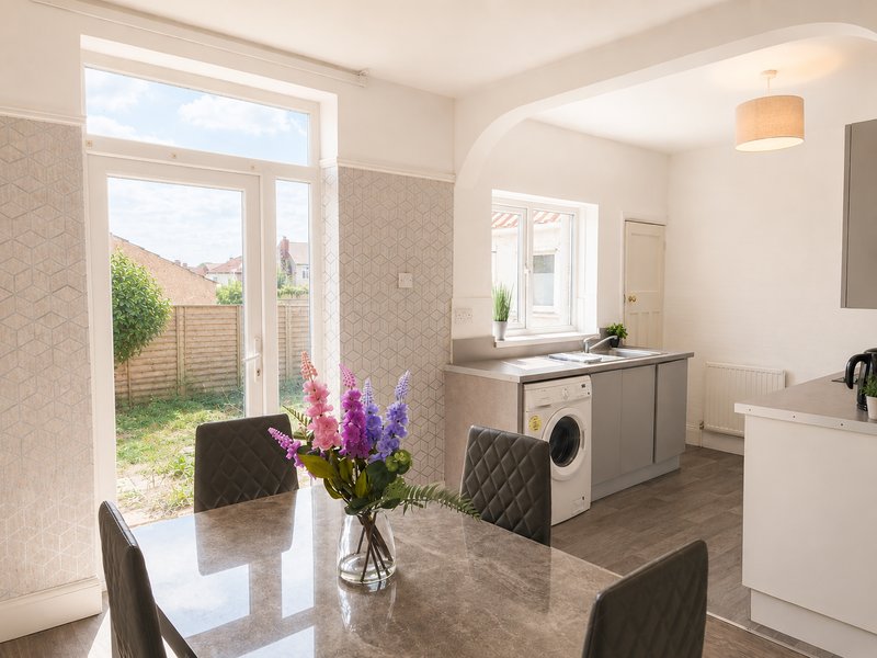 Modern kitchen-diner with grey cabinets, dining table, flowers, washing machine and garden view