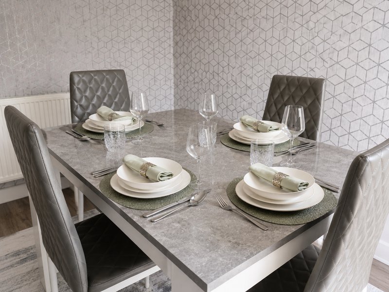 Modern dining room with gray stone table, four quilted chairs, and place settings