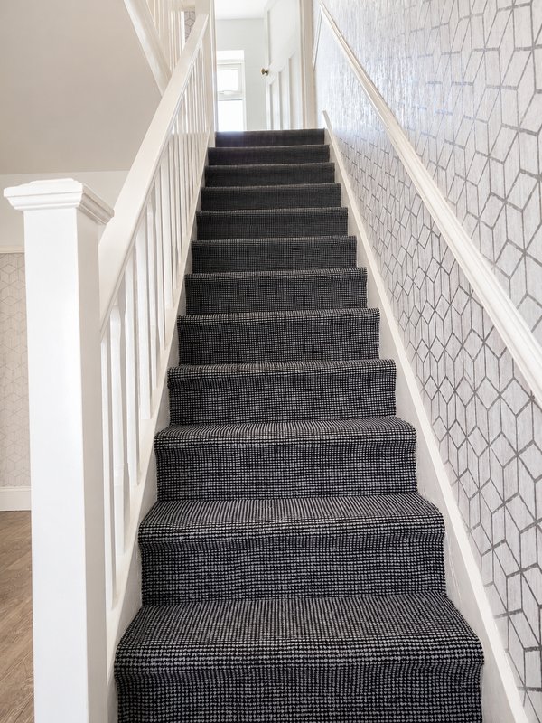 Interior staircase with dark grey carpet, white railings and geometric patterned wallpaper