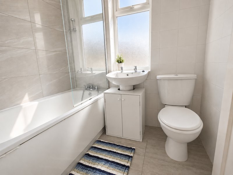 Clean modern bathroom with bathtub, pedestal sink, toilet and window