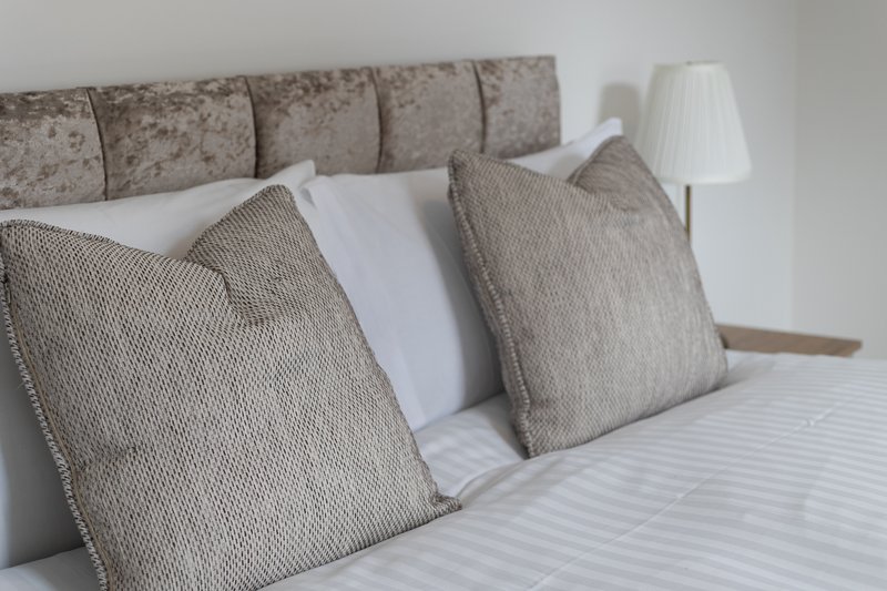 Bedroom with upholstered headboard, decorative pillows, white bedding and bedside lamp