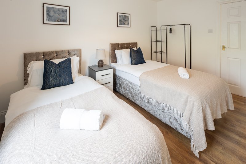 Bright twin bedroom with two single beds, wooden flooring, framed wall art, and modern furnishings.