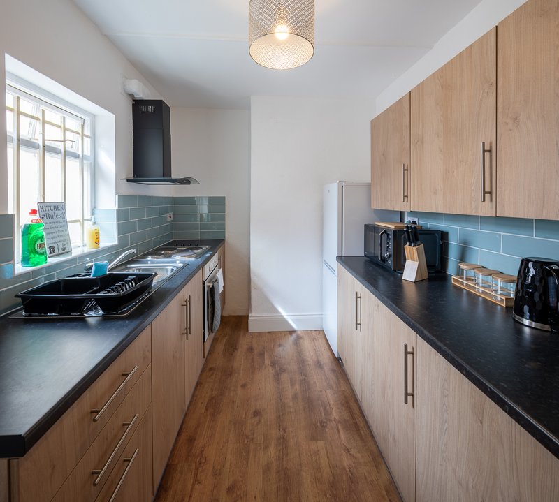 Modern galley kitchen with wooden cabinets, black countertops, blue tile backsplash and stainless steel appliances