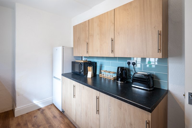 Modern kitchen with light wood cabinetry, black countertop, blue tile backsplash and appliances.
