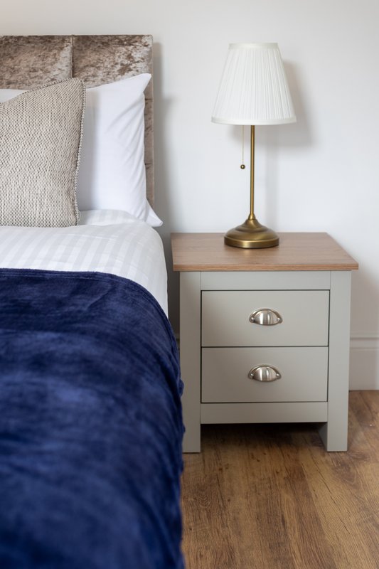Bedroom with double bed, navy duvet, bedside table with lamp and drawers