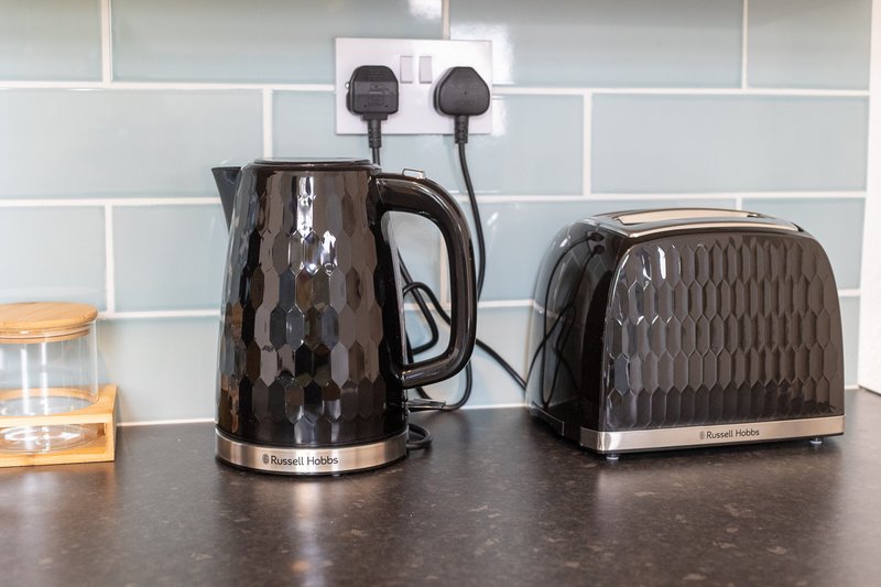 Kitchen counter with black kettle, toaster, and small appliances near white subway tiles