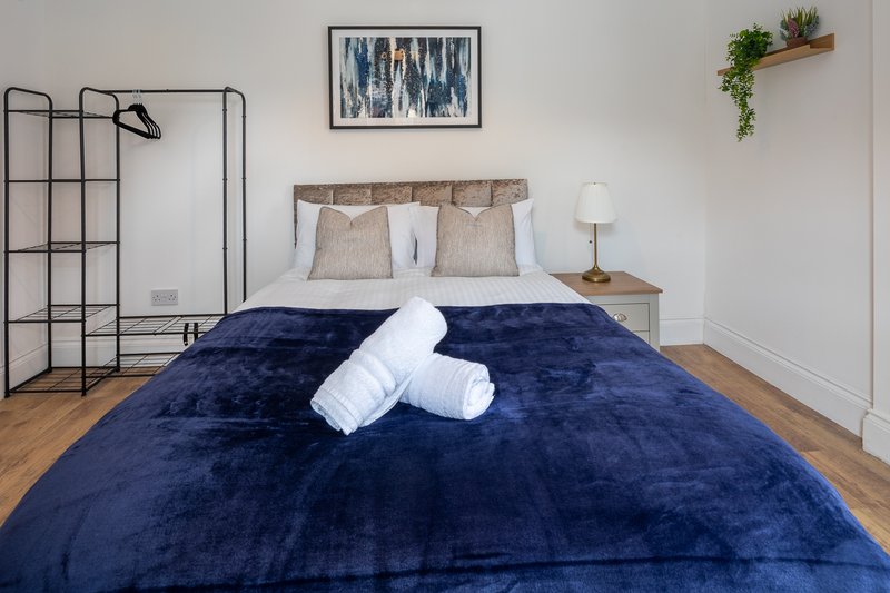 Bedroom with navy blue velvet bed, white rolled towels, wooden floor and wall art
