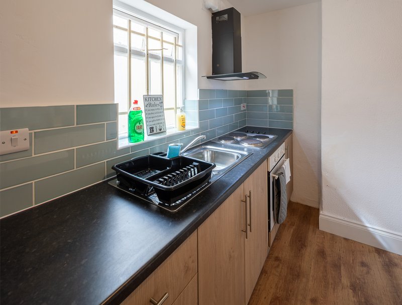 Kitchen with gas hob, black countertop, green tile splashback and window