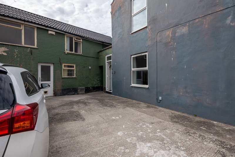 Exterior courtyard between green and dark buildings with parked car and concrete paving