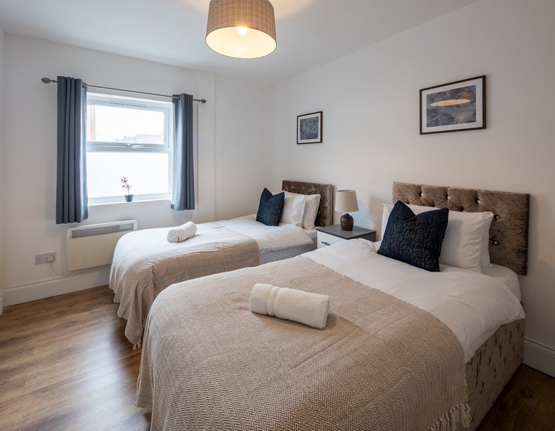 Bright bedroom with two single beds, neutral bedding, window with blue curtains, wooden floor