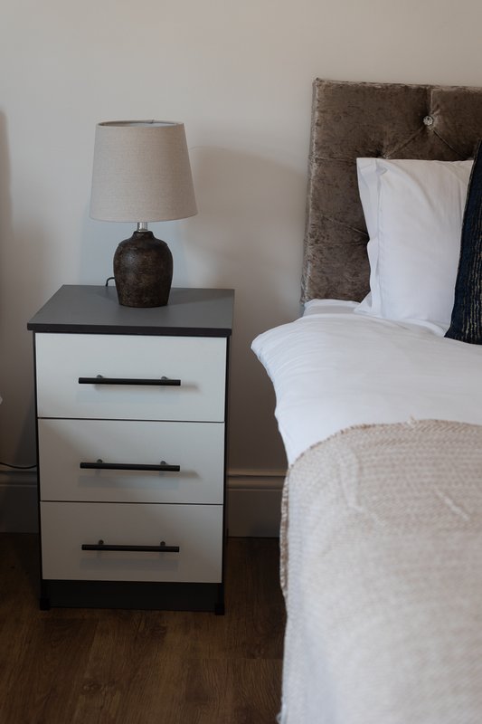 Bedroom with bedside table, lamp, and bed with white pillows and neutral bedding