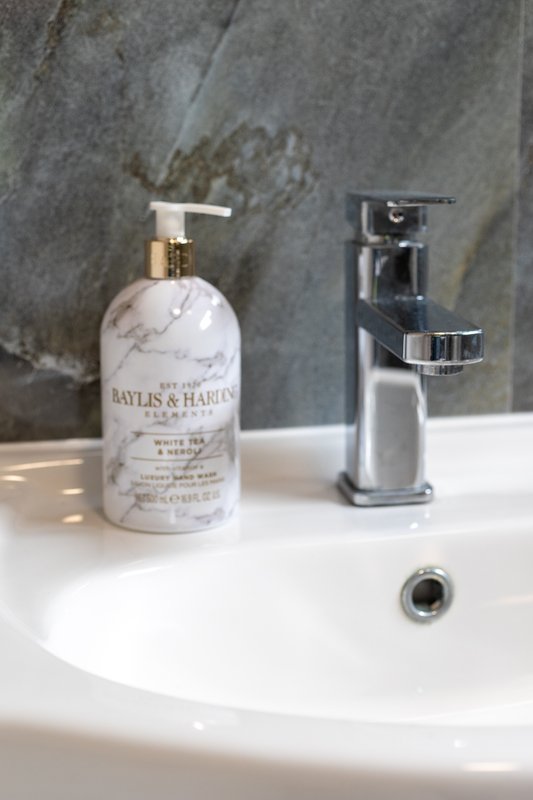 Bathroom sink with chrome faucet, soap dispenser, and gray tile backsplash