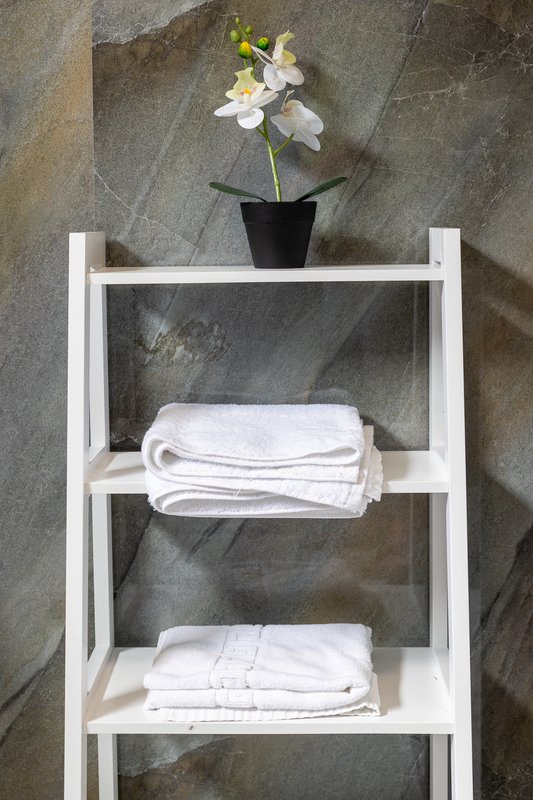 White shelving unit with folded towels, potted white flowers on top shelf