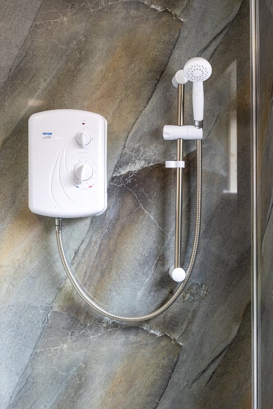 Bathroom shower with white instant water heater unit and handheld showerhead on tiled wall