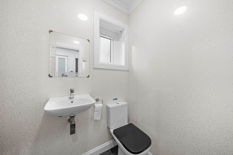 Clean bathroom with white sink, mirror, toilet, and window