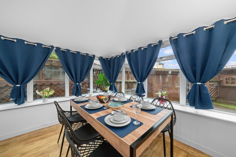 Bright dining room with wooden table, black chairs, blue curtains and large windows