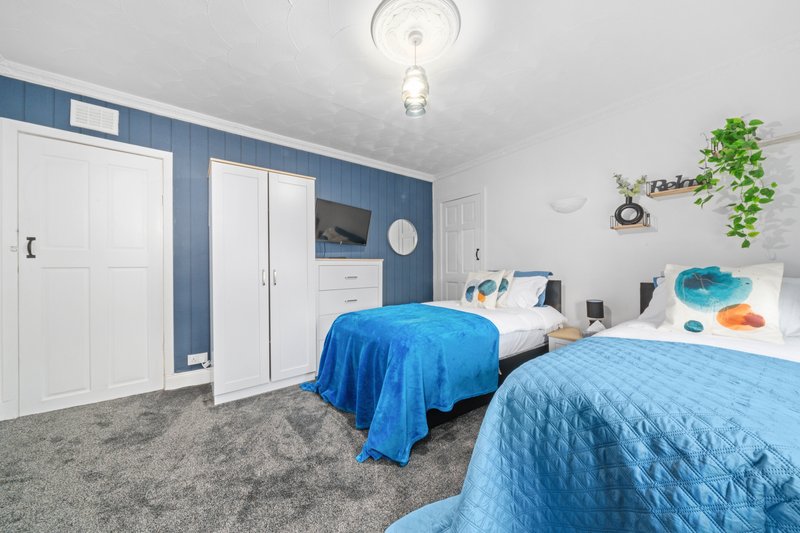 Twin bedroom with blue bedding, white wardrobes, blue accent wall, and potted plants