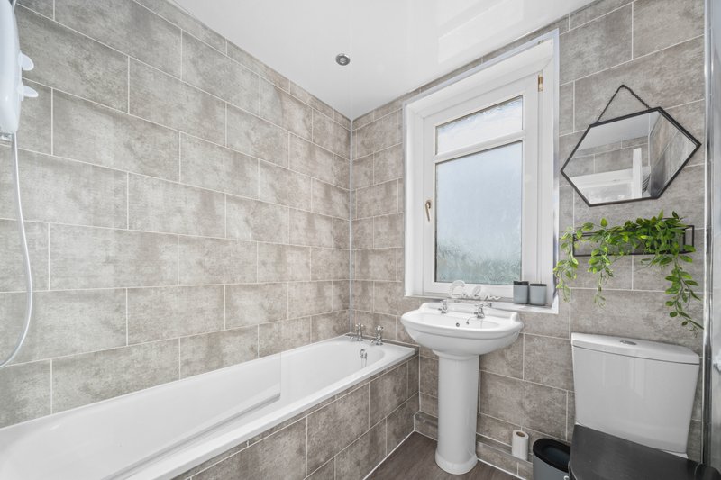 Modern bathroom with bathtub, pedestal sink, grey tile walls and window