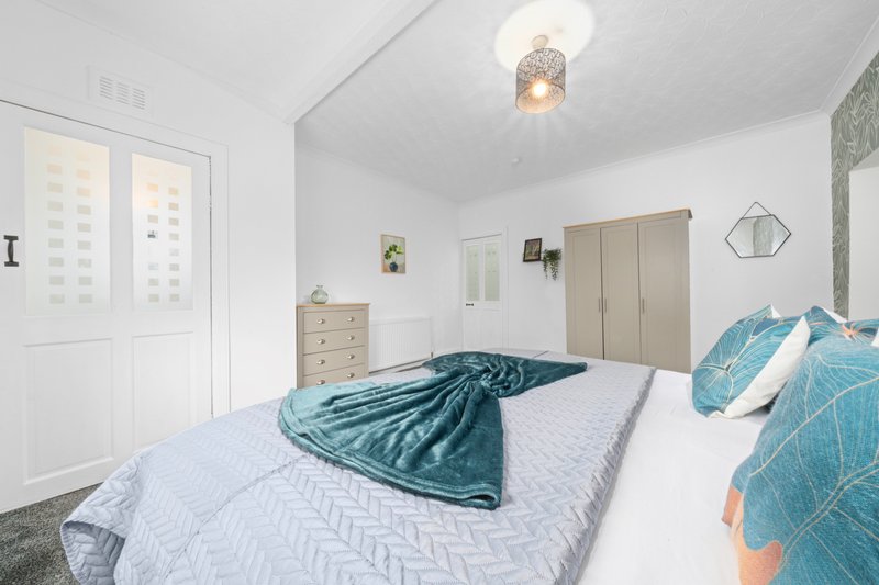 Bright bedroom with double bed, teal bedding, wooden furniture and pendant ceiling light