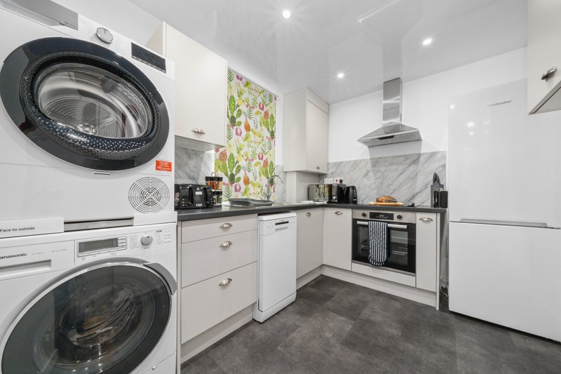 Modern kitchen with white cabinetry, stainless steel appliances, stacked washing machines, and floral artwork