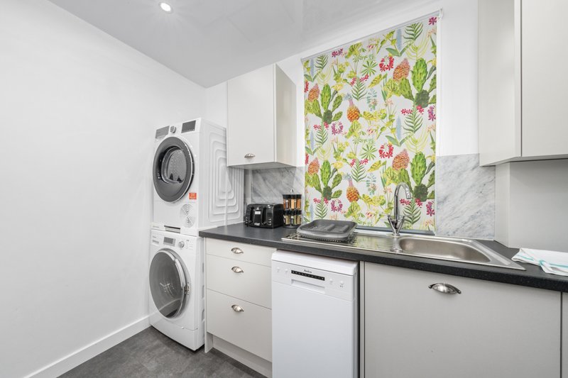 Modern kitchen with white cabinetry, stacked washer-dryer, floral backsplash and dark countertop