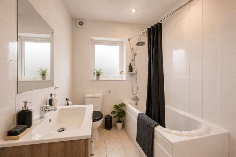 Modern bathroom with white tiles, sink, toilet, bathtub and black shower curtain