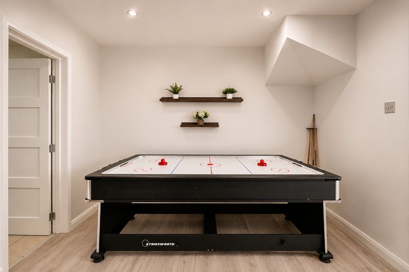 Recreation room with black air hockey table, wooden shelves with plants, and white door