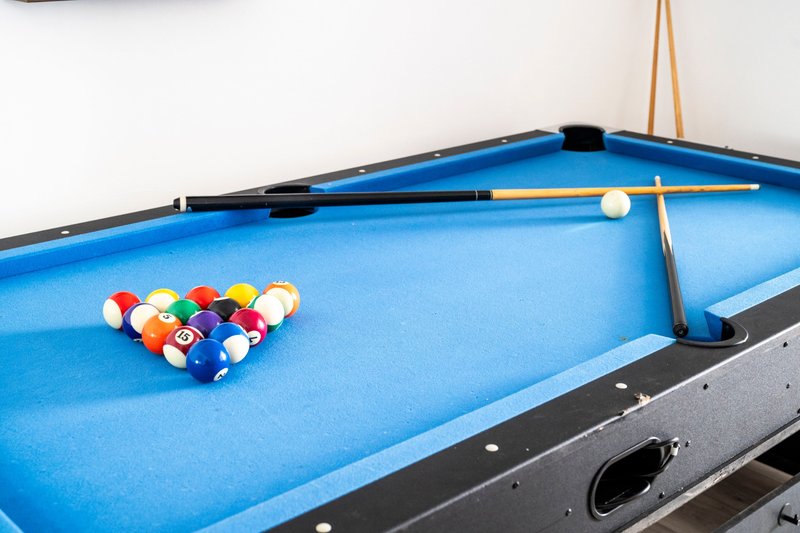 Blue pool table with cues, balls, and triangle rack set up ready for play