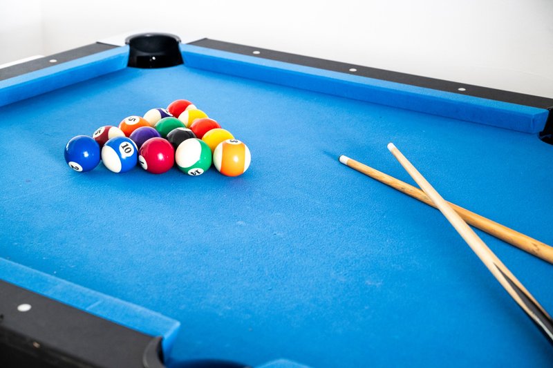 Blue pool table with billiard balls racked and two cues ready to play