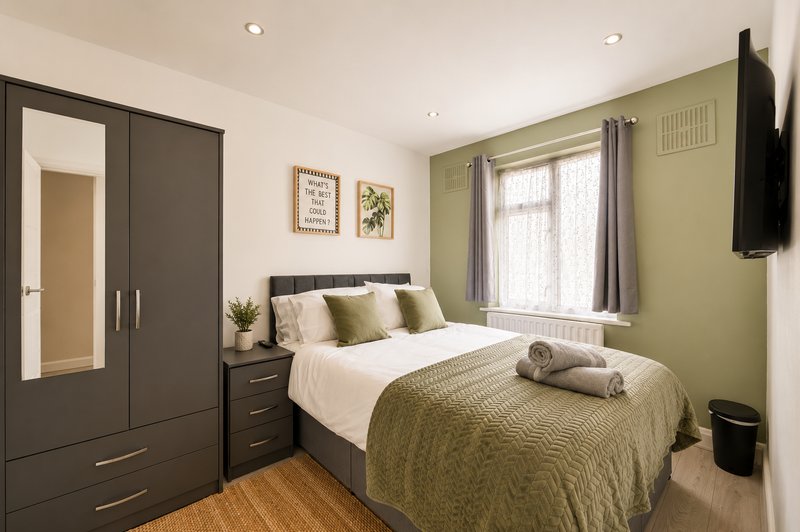 Bedroom with double bed, olive green bedding, dark wardrobe, and wall-mounted TV