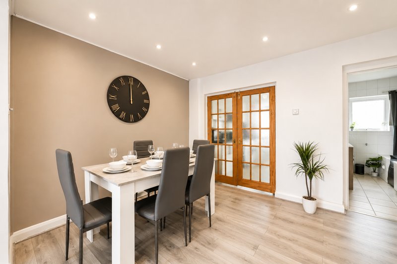 Dining area with white table, grey chairs, wall clock, wooden doors and potted plant
