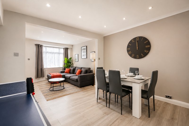 Open-plan living and dining area with sofa, dining table, chairs and large wall clock