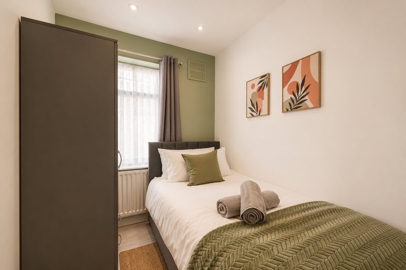 Modern bedroom with single bed, green accent wall, window with curtains and wall art