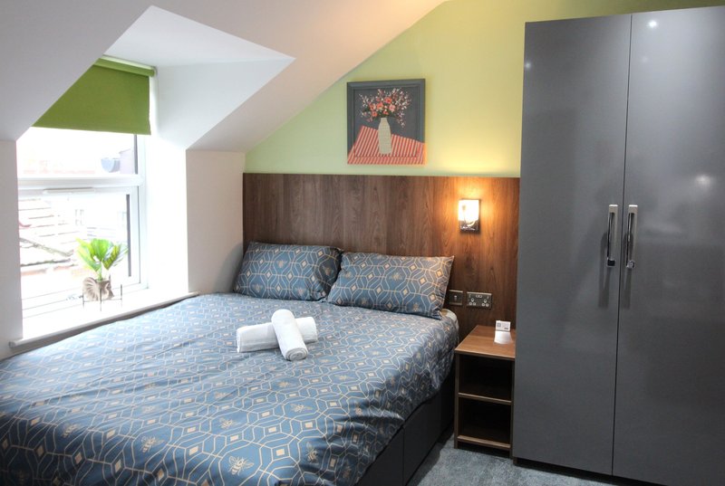 Attic bedroom with double bed, wooden headboard, gray wardrobe and skylight window