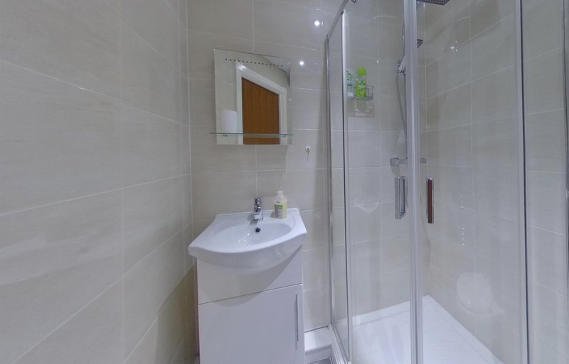 Modern bathroom with white curved sink, mirror, and walk-in shower enclosure